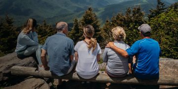 A multi-generational family sits together looking out over the moutains