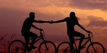 couple on bikes during sunset holding hands.